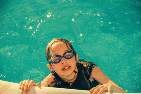 Little girl in swimming pool. Summer outdoor. The girl swims in the pool wearing swimming goggles.の写真素材