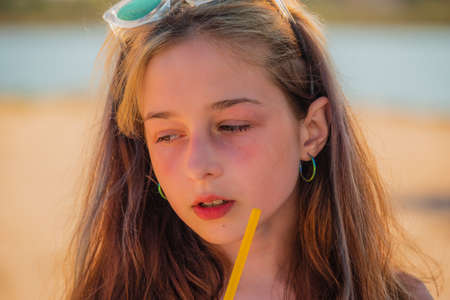 Girl in sunglasses drinks from a straw a drink on the sea on the beach.