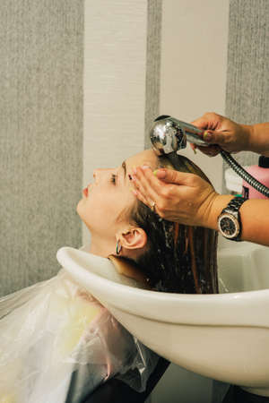 Hairdresser making a hair style to cute little girl. A teenage girl has her bangs lightened in a...