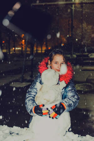 happy child girl plaing with a snowman on a snowy winter walk. The girl was making a snowman....