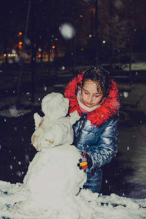 happy child girl plaing with a snowman on a snowy winter walk. The girl was making a snowman....
