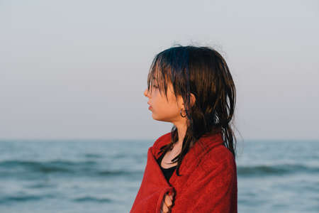 Teenager girl in a towel by the sea at sunset. Girl in a red towel. Rest, vacation, childhood.Sunsetの写真素材