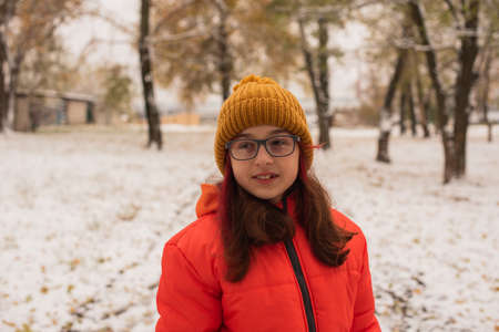 a girl in a bright orange warm jacket. Girl in an orange jacket in snowy weather. Teenager girl in winterの写真素材