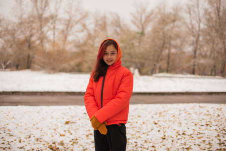 a girl in a bright orange warm jacket. Girl in an orange jacket in snowy weather. Teenager girl in winterの写真素材