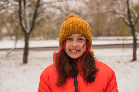 a girl in a bright orange warm jacket. Girl in an orange jacket in snowy weather. Teenager girl in...