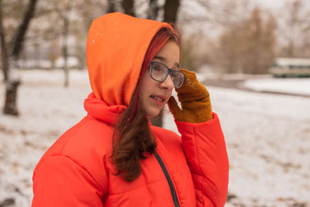 a girl in a bright orange warm jacket. Girl in an orange jacket in snowy weather. Teenager girl in...