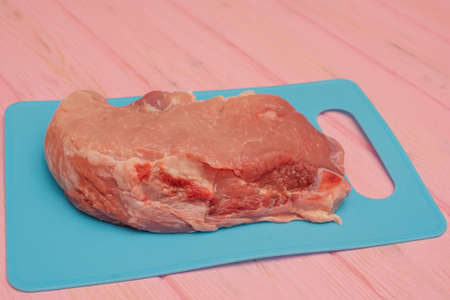 Pink raw pork steaks lie on a blue board. Appetizing meat. Pork on blue board on pink background