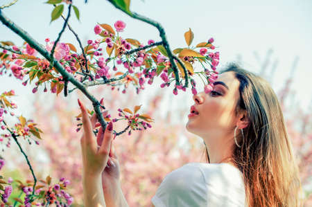 Young beautiful girl with long hair enjoys the beauty of spring nature near the blossoming sakura