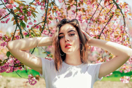 Young beautiful girl with long hair enjoys the beauty of spring nature near the blossoming sakura