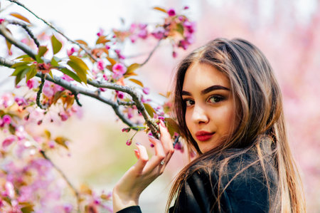 girl with long hair enjoys the beauty of spring nature near the blossoming sakura tree.の写真素材