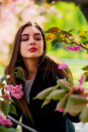 girl with long hair enjoys the beauty of spring nature near the blossoming sakura tree.の写真素材