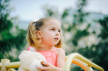 Adorable girl in dress swing on playground in park. Little girl in dress on the playground in summerの写真素材