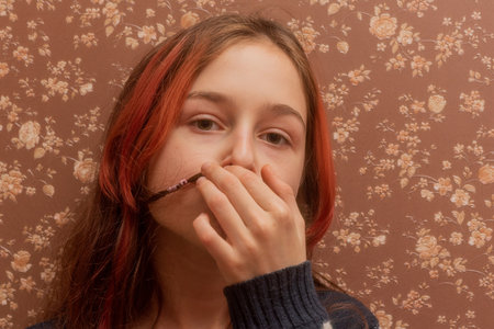 Teenager at home portrait.A young girl with red strands of hair on a background of brown wallpaper