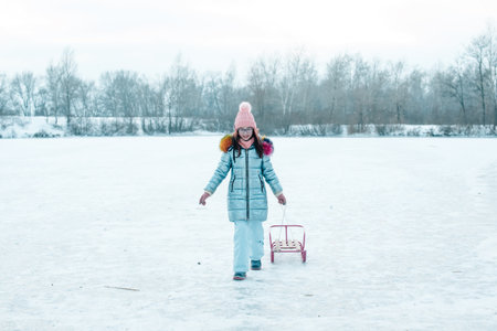 Winter walk. Beautiful caucasian girl on ice in the snow. Girl in a pink hat and coat. Winterの写真素材