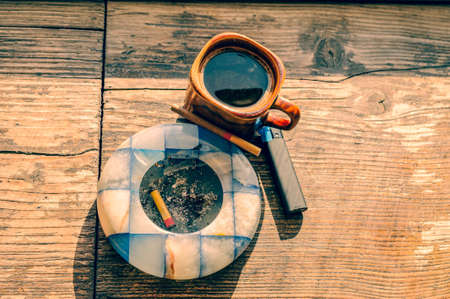 coffee time. Coffee and cigarette with lighter and ashtray on the wooden table. Symbol of bad habitsの写真素材