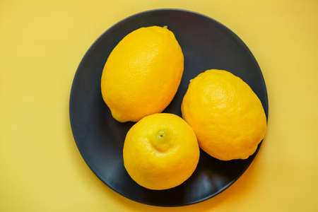 Three lemons on a black plate on a yellow background. Background. citrus fruit juice,の写真素材