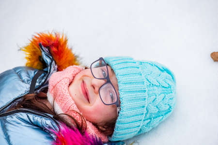 Winter, young girl in warm clothing. Teenage Girl. The child lies in the snow. Child with glassesの写真素材