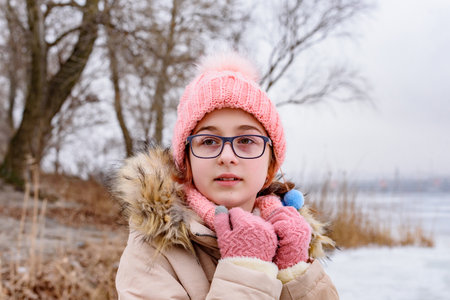 Portrait of teenage girl in pink hat and coat standing in winter landscape. cute girl with glassesの写真素材
