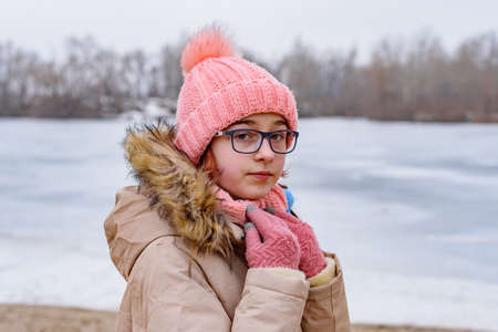 Portrait of girl in pink hat and coat standing in winter landscape. girl with glasses. riverの写真素材