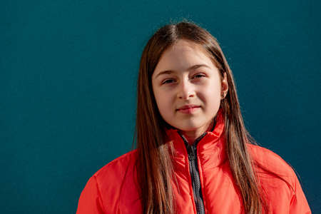photo of teenage girl on a turquoise wall background. Teenager girl in orange jacket. portrait,の写真素材