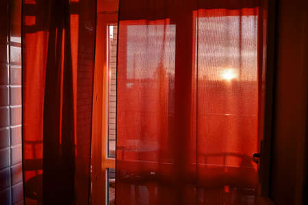 Through the curtain shines the setting sun. The setting sun shines through the window through the curtainsの写真素材