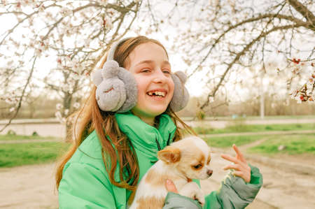 Teenage girl in a green jacket with a chihuahua puppy in her arms in the spring. trees are bloomingの写真素材