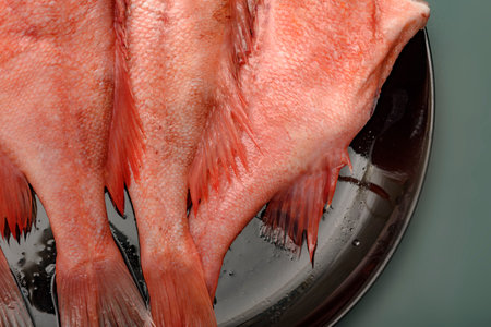 The split sea bass on a round plate black. Raw red sea bass.