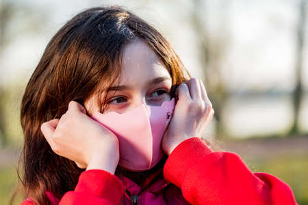 Teenage girl in a protective mask made of pink fabric on the street.の写真素材