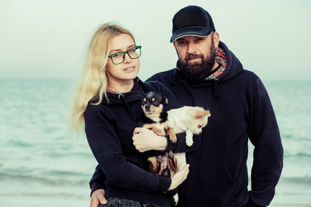 Man and woman in hoodie near the sea. Family and pets concept, two Chihuahua breed dogs. vacations,...