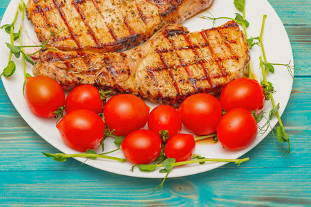 Two grilled pork steaks on a plate with sprouted chickpeas and tomatoes on a turquoise background.の写真素材