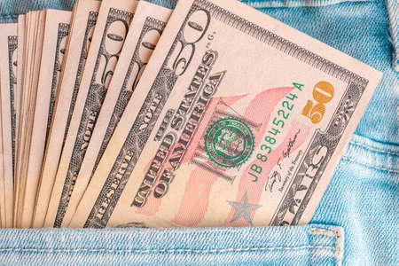 Macro shot of trendy jeans with US dollar bills in a pocket. Dollars in jeans. Financial concept.