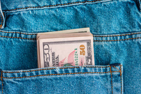 Macro shot of trendy jeans with US dollar bills in a pocket. Dollars in jeans. Financial concept.