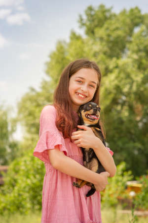 A teenage girl with a Chihuahua dog in her arms is smiling on a blurred background of trees.の写真素材