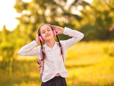 Beautiful little girl listening to music on headphones in autumn park. Schoolgirl in outdoors.の写真素材