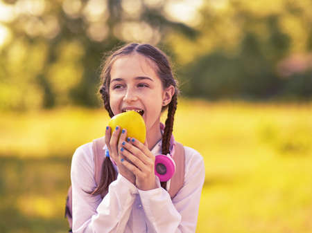 Young beautiful girl bites an apple. Schoolgirl girl eating an apple in nature.の写真素材