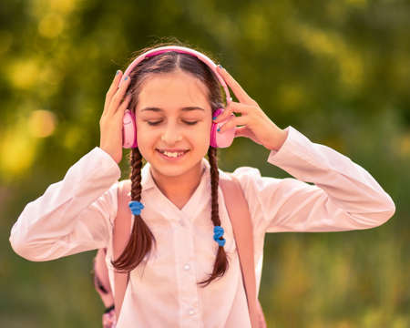 Outdoor portrait of beautiful teenage girl listening music with wireless headphones. Schoolgirlの写真素材
