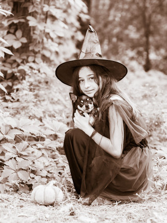 Shot of a little girl in halloween costume posing with pumpkin outdoor. Teenage girl with a dog.の写真素材