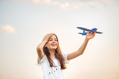 Young teenage girl holding airplane. Toy plane on the background of the sky in hand. Dream. Freedomの写真素材