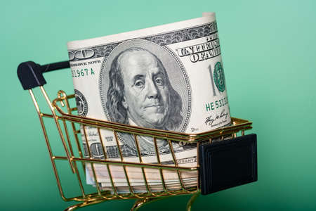 financial concept. Money dollars in a gold colored shopping cart on a light green background.の写真素材