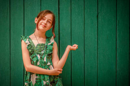 Girl 10 or 11 years old on a summer day. Teen girl portrait in a dress on a green background.の写真素材