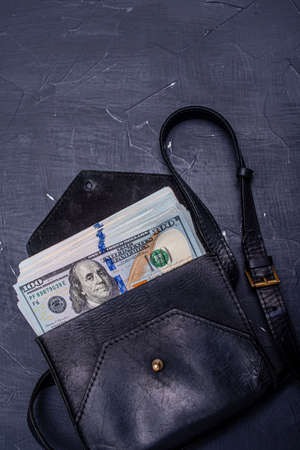 Paper money dollars in a black leather bag on a black background. The concept of buying, storing savings.の写真素材