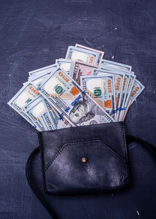 financial and business concept. Dollars in a black leather bag on a black cement background.