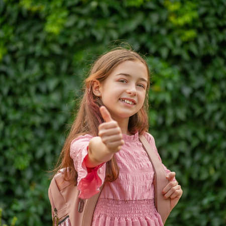 Teen girl in a pink dress with a backpack. The girl shows like gestures.の写真素材