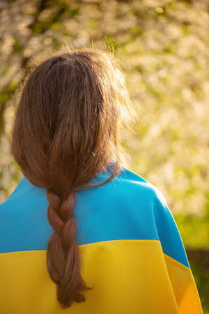 The girl is standing behind the camera with the Ukrainian flag on her back. Yellow and blue fabric.の写真素材