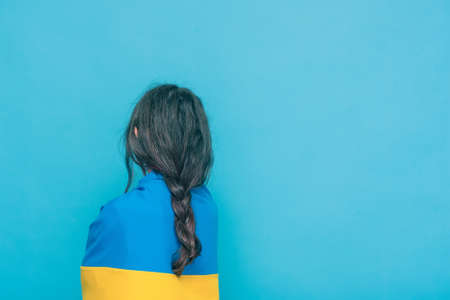 Photo of a girl with a braid on a blue background. Yellow with blue fabric on the shoulders.