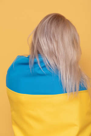Woman back to camera on a yellow background. Woman with blue-yellow cloth on her shoulders.の写真素材