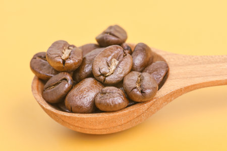 Wooden spoon with aromatic roasted coffee beans on a yellow backgroundの写真素材