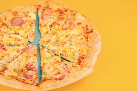 Pizza with chicken, ham and corn on a turquoise plate on a yellow backgroundの写真素材
