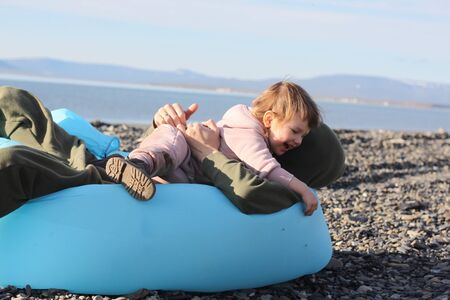 Father and daughter resting on an inflatable sofa on an empty beach over the sea. lamzac. Travel,...
