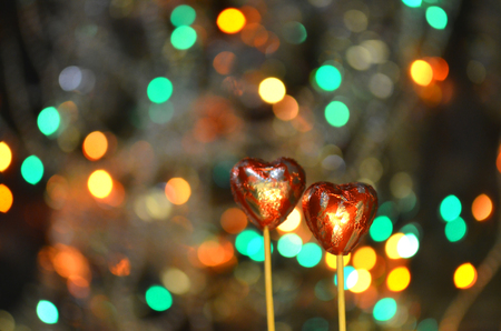 Chocolate candies for valentine's day. Red heart shape chocolate on lolly stick. Chocolate heart in red foil on a stick on a bokeh blurred backgroundの写真素材